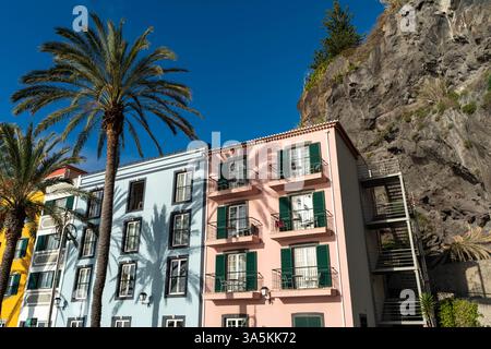 Case costiere colorate vicino a una scogliera rocciosa con palme Foto Stock