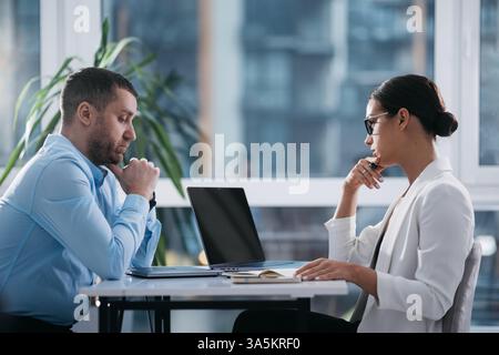Due professionisti di mezza età impegnati, uomini e donne, leader aziendali, partner che controllano la lettura di documenti e rapporti finanziari, collaborando con un notebook Foto Stock
