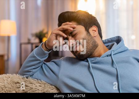Uomo indiano malato che sfrega templi per curare il mal di testa, soffre di tensione, emicrania, stress e pressione alta a casa. L'ispanico tiene la testa, soffre di dolore, soffre di grave disagio. Foto Stock