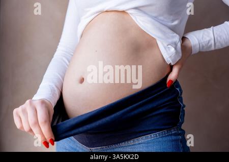 Primo piano della pancia di una donna incinta che indossa pantaloni elastici in denim Foto Stock