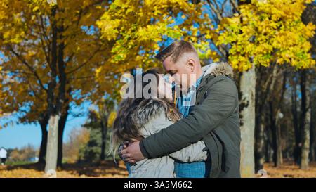 Coppia amorevole che abbraccia tra gli alberi lievitati dorati durante il luminoso pomeriggio autunnale Foto Stock