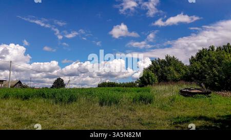 Paesaggio rurale estivo con campo verde, alberi, cielo blu e nuvole spettacolari. Tradizionale scenario di campagna con edifici rustici in Ucraina. Foto Stock