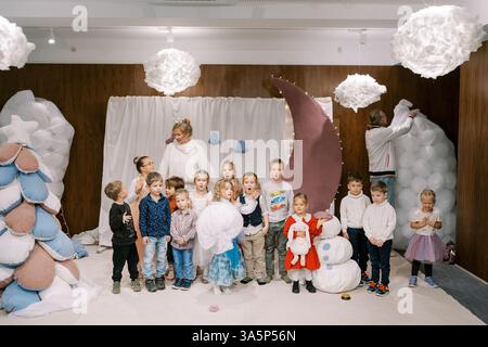 Ucraina, Leopoli - 4 marzo 2025: Bambini in piedi sul palco di un asilo con attori vicino a decorazioni sotto forma di un albero di Natale e un Foto Stock