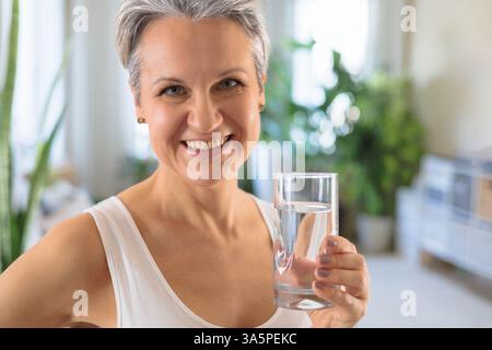 Felice sorridente donna matura di mezza età con capelli grigi che fa esercizi a casa, facendo yoga Foto Stock