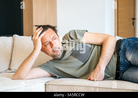 Uomo adulto contemplativo che si stende sul divano e pensa, attenzione selettiva Foto Stock