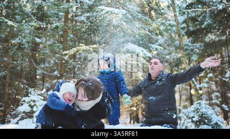 La famiglia felice si diverte a trascorrere momenti divertenti sulla neve, circondato da una splendida foresta invernale piena di alberi e fiocchi di neve che cadono Foto Stock