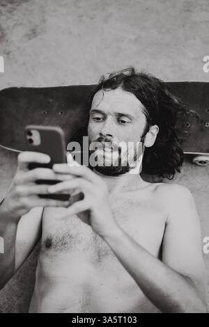 Uomo che utilizza smart phone mentre giaceva sul sedile a skate park Foto Stock
