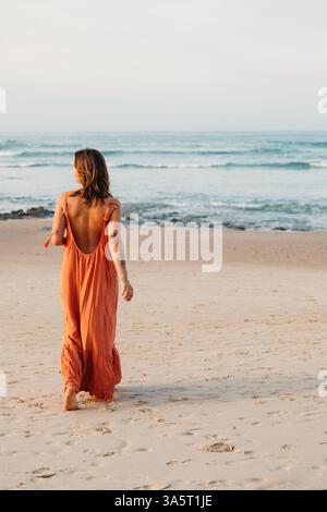 Giovane donna con un vestito sciolto che cammina a piedi nudi sulla spiaggia Foto Stock