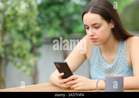 Donna seria seduta in terrazza con lo smartphone a casa Foto Stock
