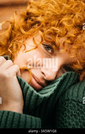 Ritratto ravvicinato di una donna rossa sorridente che si rilassa e tiene in mano il suo maglione verde caldo Foto Stock