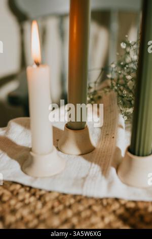 Tre candele sono accese su un tavolo, di cui una verde. Le candele sono posizionate su un panno bianco e la candela verde è la più alta. Concetto Foto Stock