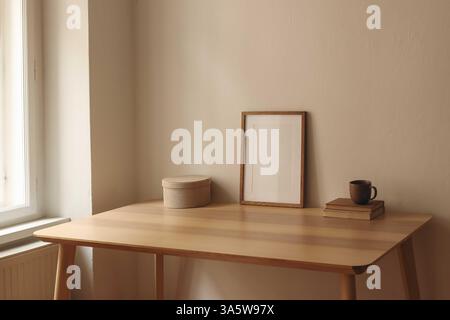 Eleganti interni scandinavi, soggiorno. Mockup di cornice in legno vuoto sul tavolo alla finestra. Vecchi libri, scatola rotonda. Tazza di caffè, tè. Alla moda Foto Stock