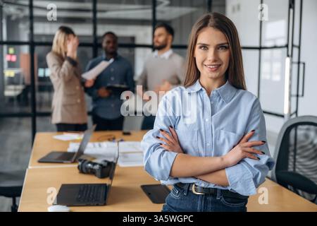 Una donna allegra è in piedi. I lavoratori professionisti si trovano in un ufficio moderno insieme. Foto Stock
