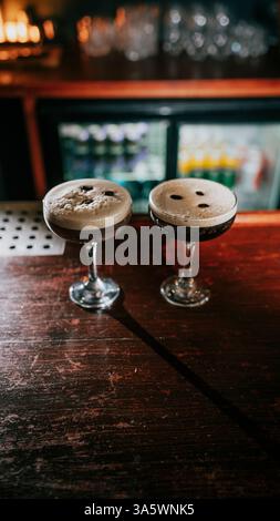 Due bicchieri di liquido marrone su un bancone di legno. I bicchieri sono riempiti con un liquido scuro e hanno un piccolo foro al centro Foto Stock