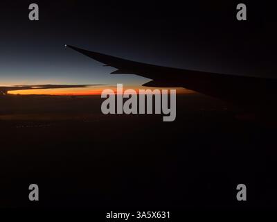 Vista aerea dall'aereo del tramonto arancione scuro. L'ala dell'aereo è leggermente visibile. Le nuvole sono visibili all'orizzonte. Foto Stock