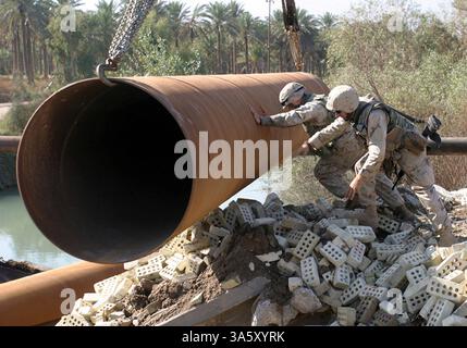 13 novembre 2004; Lutafiyah, IRAQ; Un marinaio e marine assegnato alla 24th Marine Expeditionary Unit (24th MEU) guidano un tubo in un fiume a Lutafiyah, Iraq. I tubi sono stati utilizzati come base per un ponte ricostruito che è stato gravemente danneggiato in ripetuti attacchi da parte di militanti anti anti-iracheni. Il 24° MEU sta attualmente conducendo operazioni di sicurezza e stabilità nella provincia di Babil settentrionale. Foto Stock