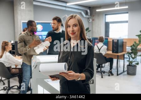 La donna è davanti ai colleghi. Le persone sono in ufficio vicino alla stampante 3D. Foto Stock