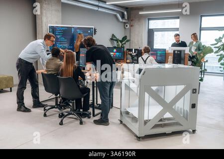 Grande schermo con codice sul muro. Le persone sono in ufficio vicino alla stampante 3D. Foto Stock