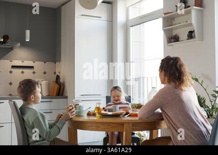 Vista grandangolare della ragazza Happy con sindrome di Down che fa colazione con la famiglia a casa mentre si siede insieme a un tavolo di legno e si copia lo spazio Foto Stock
