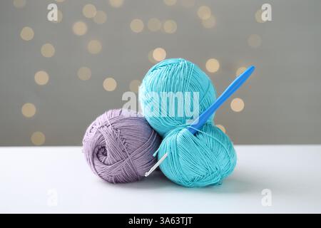 Filati colorati e uncinetto sul tavolo bianco su sfondo grigio con luci sfocate, effetto bokeh Foto Stock