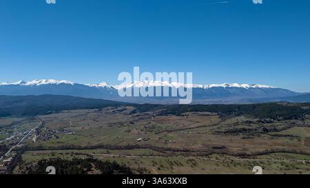 Splendida vista aerea della montagna innevata di Rila che torreggia su una pittoresca valle in Bulgaria, bagnata dalla calda luce del sole di una limpida giornata primaverile Foto Stock