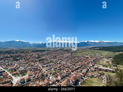 Vista aerea della città di Razlog in Bulgaria, con le montagne innevate di Pirin e il cielo azzurro, durante una splendida giornata di primavera Foto Stock