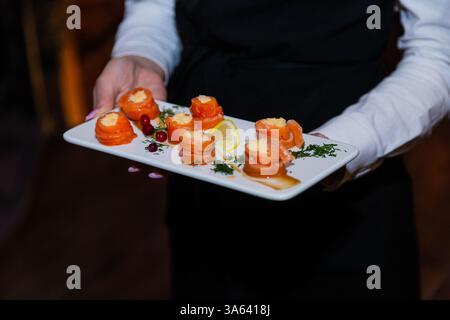 Appetitosi involtini di pesce nelle mani di un cameriere su un piatto bianco. Pesce rosso ripieno. ampia vista Foto Stock