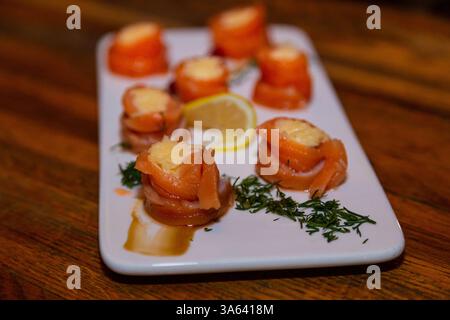 Appetitosi involtini di pesce rosso con ripieno all'interno su un piatto bianco e un tavolo di legno in un ristorante. ampia vista laterale Foto Stock