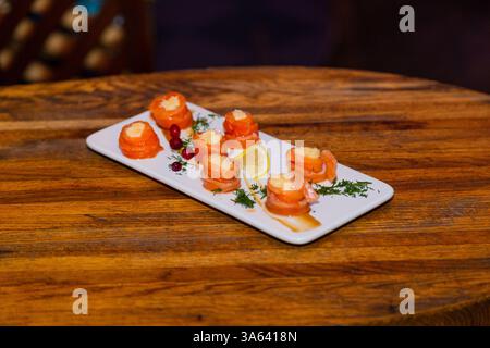 Appetitosi involtini di pesce rosso con ripieno all'interno su un piatto bianco e un tavolo di legno in un ristorante. vista dall'alto Foto Stock
