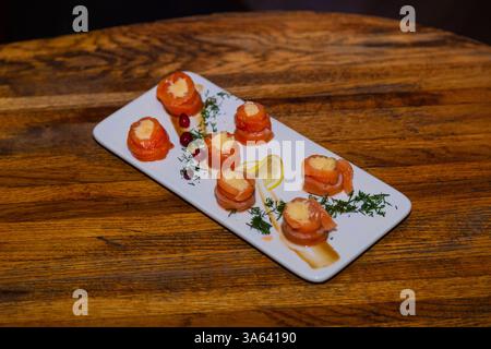 Appetitosi involtini di pesce rosso con ripieno all'interno su un piatto bianco e un tavolo di legno in un ristorante. Cibo gustoso Foto Stock
