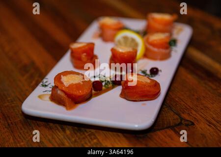 Appetitosi involtini di pesce rosso con ripieno all'interno su un piatto bianco e un tavolo di legno in un ristorante. Cibo delizioso a base di pesce. Cucina asiatica Foto Stock