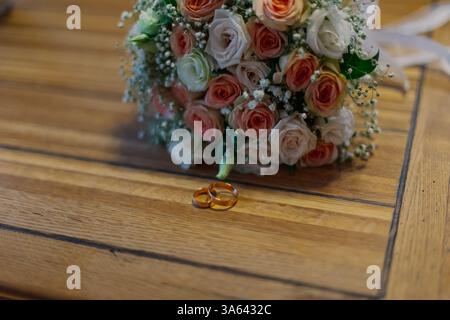 Un mazzo di fiori freschi fatti a mano giace su un tavolo di legno su cui giacciono le fedi nuziali in questo felice giorno. dettagli per matrimoni Foto Stock