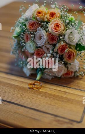 Un mazzo di fiori freschi fatti a mano giace su un tavolo di legno su cui giacciono le fedi nuziali in questo felice giorno Foto Stock
