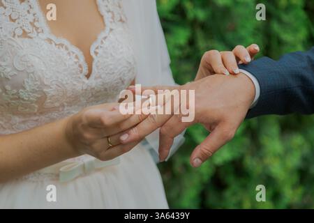 Una bella giovane sposa mette un anello nuziale al dito dello sposo il giorno del suo matrimonio, sono felici Foto Stock