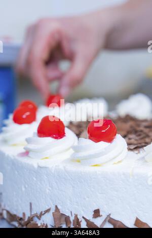 La torta con ciliegie, cioccolato e panna è decorata a mano, la cottura delle torte, Haselstaller Hof Cafe Kuh, Wildberg, Foresta Nera, Germania, Europa Foto Stock