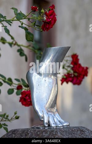 Piede di una donna in punta di piedi, scultura color argento, metallo lucido, rose rosse sullo sfondo, Steinbach, Michelstadt, Odenwald, Assia, Germania, E. Foto Stock