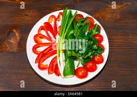 Peperoni rossi brillanti, pomodori maturi, erbe fresche e cipolle verdi sono disposti in modo splendido su un piatto bianco. Questo vivace display mostra il fr Foto Stock