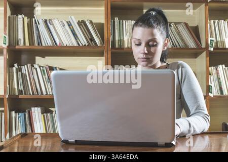 Ragazza dello studente e il computer portatile in una libreria vintage Foto Stock