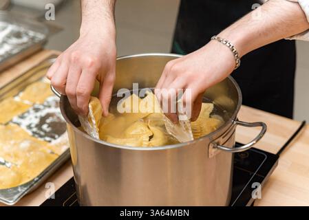 Uno chef posiziona con cura ravioli freschi fatti in casa in una pentola d'acqua bollente su una stufa a induzione in una cucina professionale. Foto Stock