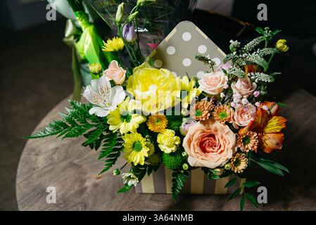 Vivace composizione floreale mista in una confezione regalo a righe con rose, margherite, vegetazione e fiori primaverili per festeggiare o decorare. Foto Stock