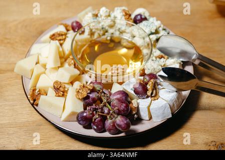 Elegante tagliere di formaggi con formaggi assortiti, uva fresca, noci e una ciotola di miele per intrattenere gourmet o abbinamenti di vini. Foto Stock