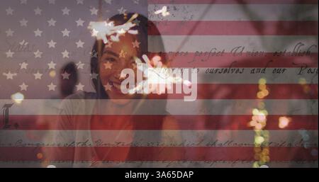 Sventolando bandiera americana e testo costituzionale contro una donna che si diverte con gli scintillanti in spiaggia Foto Stock