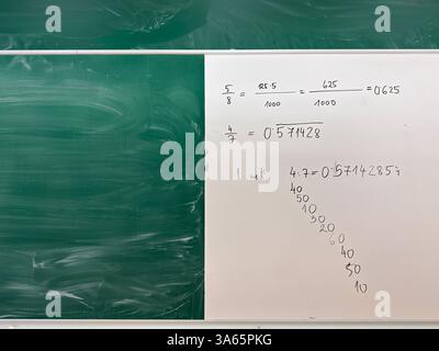 Una doppia disposizione della lavagna in aula con una lavagna verde e una lavagna bianca con frazioni matematiche scritte a mano, conversioni decimali e una lunga divisione Foto Stock