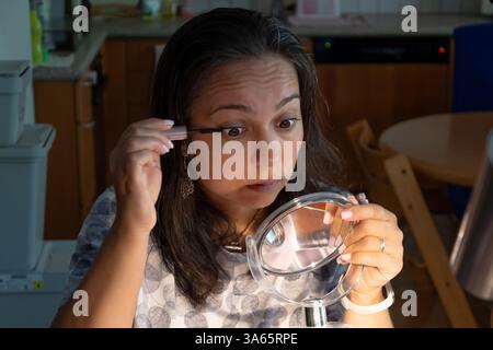 Una donna applica con attenzione il mascara alle ciglia usando uno specchio nel comfort della sua casa Foto Stock