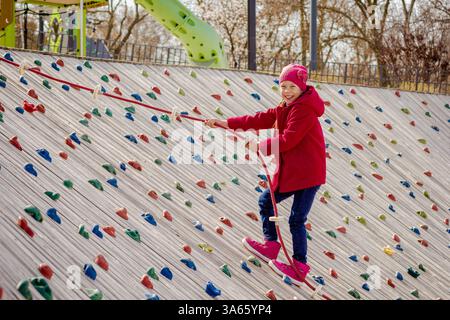 Bambino felice che si arrampica su una parete di roccia artificiale nel parco giochi Foto Stock