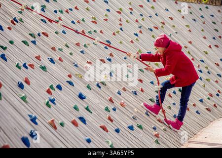 Bambino felice che si arrampica su una parete di roccia artificiale nel parco giochi Foto Stock