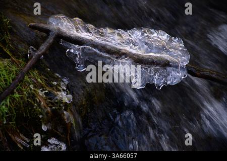 Foto ravvicinata dell'arte astratta del ghiaccio sul ramoscello di fronte alla cascata. Immagine chiave bassa con spazio di copia. Foto Stock