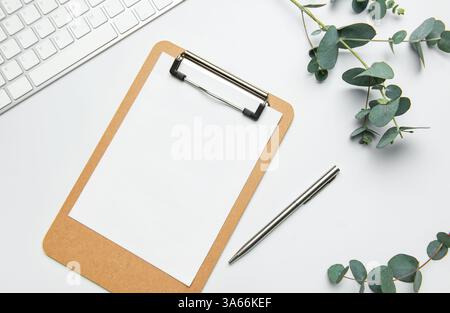 Scrivania da ufficio con appunti vuoti, tastiera, penna e rami di eucalipto su sfondo bianco Foto Stock