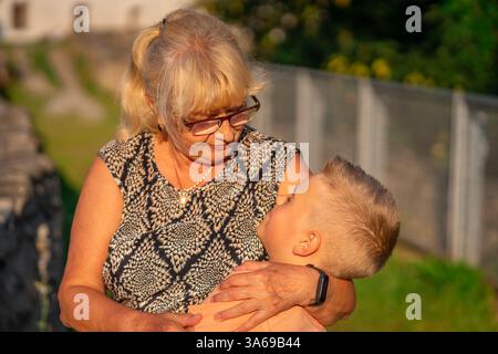 La nonna con gli occhiali abbraccia suo nipote nel parco a piedi Foto Stock