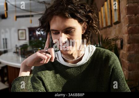 Un bel ragazzo si rilassa in un caffè alla moda, chiacchierando casualmente al telefono. Foto Stock